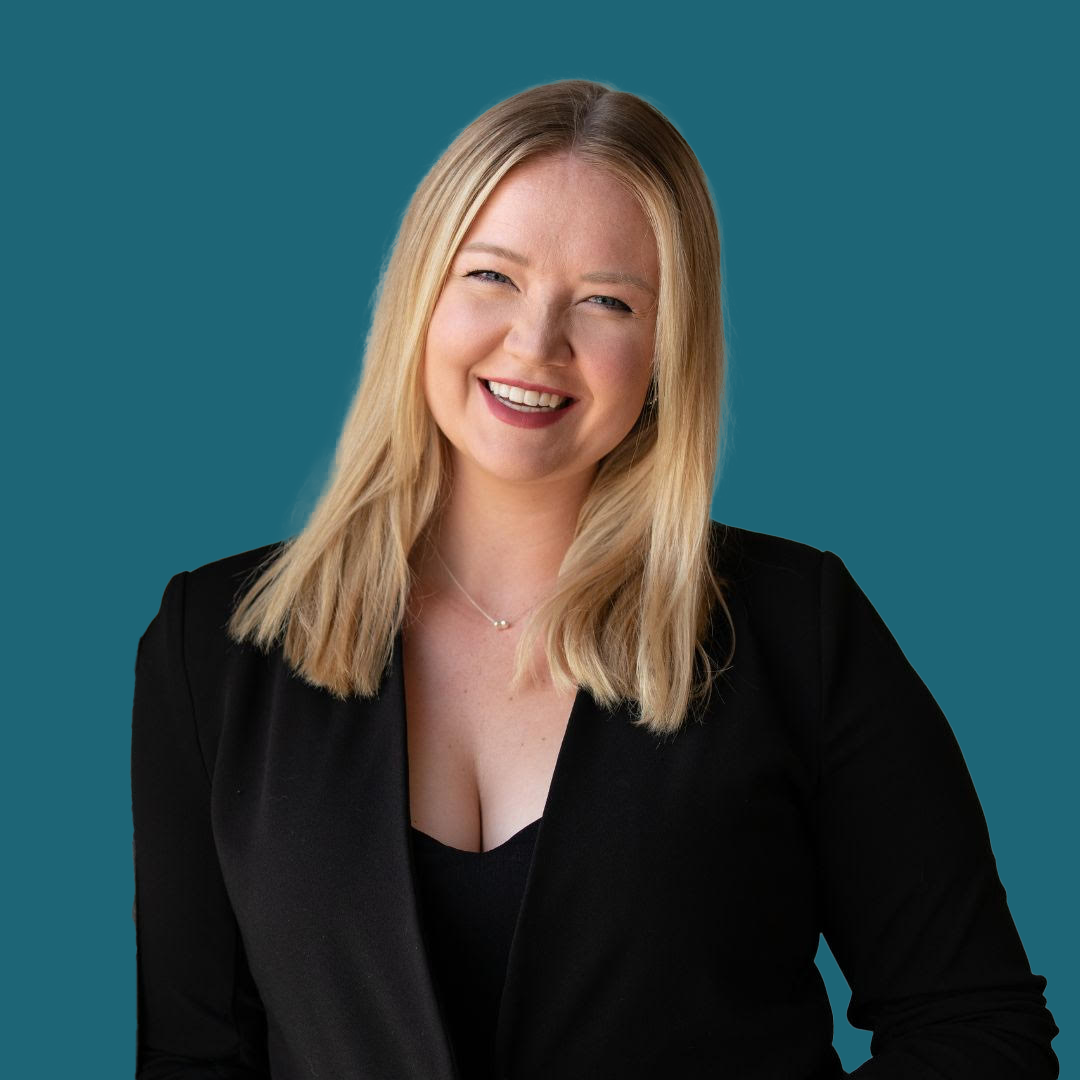 A woman in a black jacket is smiling and standing in front of a blue background.
