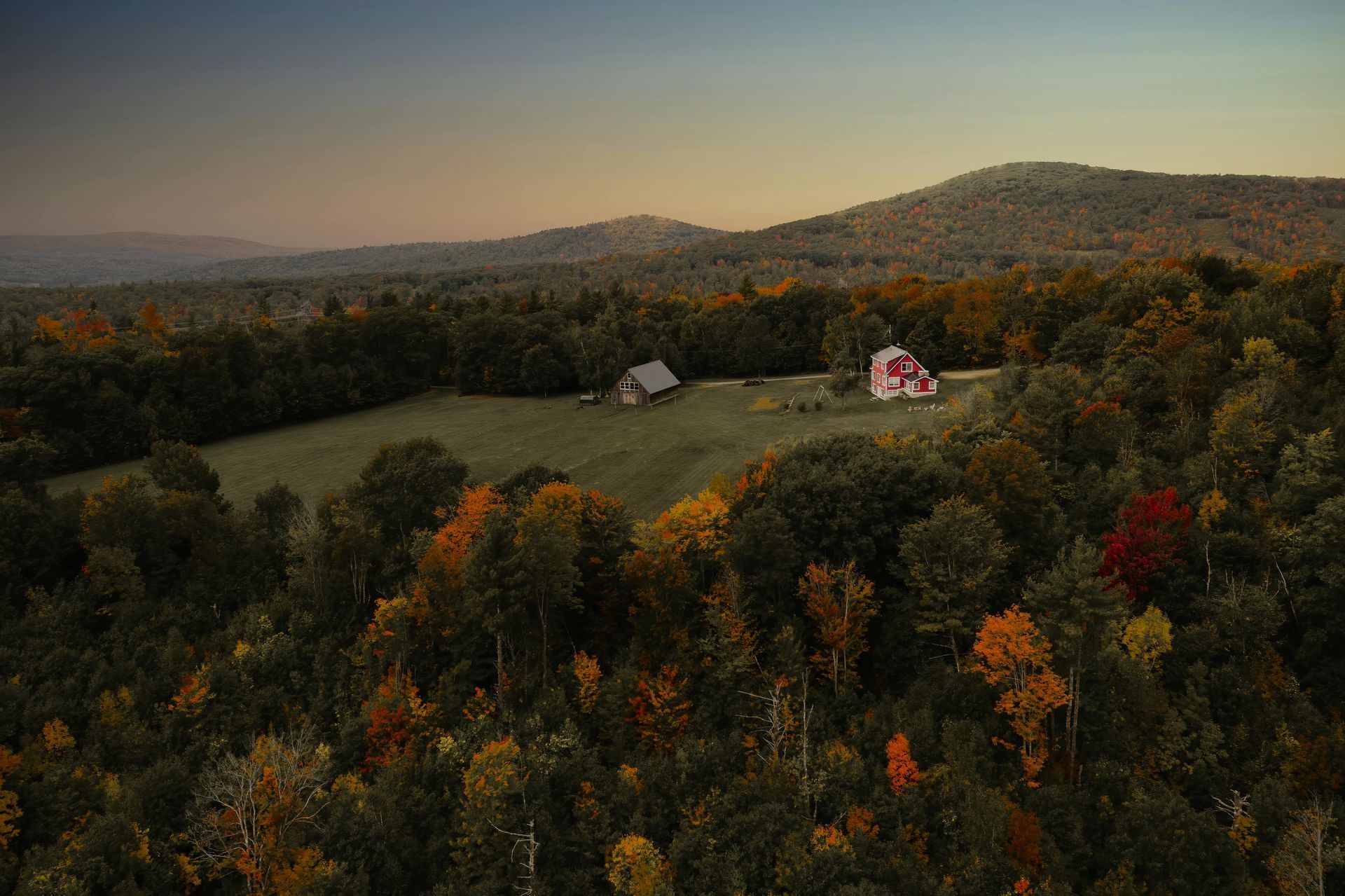 An aerial view of a barn in the middle of a forest with mountains in the background.