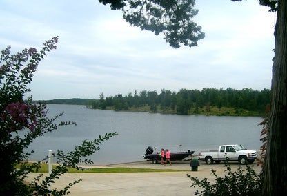A lake scene with a boat and truck at a boat ramp. Trees frame the water and sky.