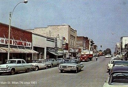 Main Street in Milan, Tennessee, 1961: Cars parked along a street with shops and businesses. Red and white awnings.