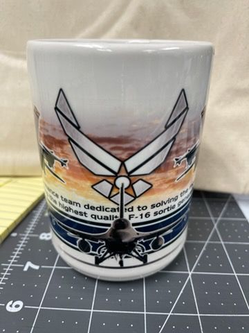 A white mug featuring the U.S. Air Force logo, an F-16 jet, and text about providing high-quality sortie performance.