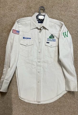 A white button-down long-sleeve western shirt with an American flag patch, name tag, logo, and letter W on the sleeves.