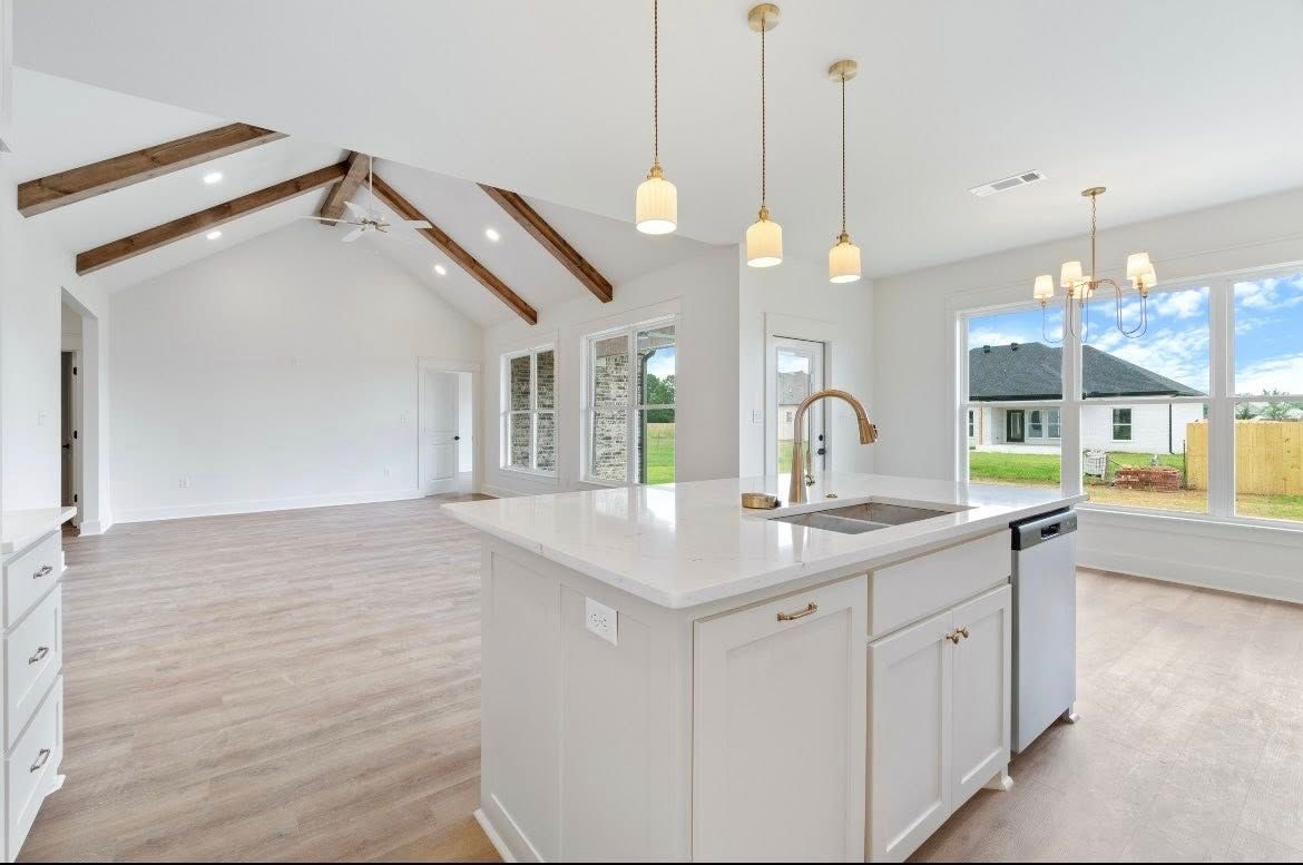 A modern, open-concept kitchen and living area with white cabinets, a large island, vaulted ceilings, and wooden beams.