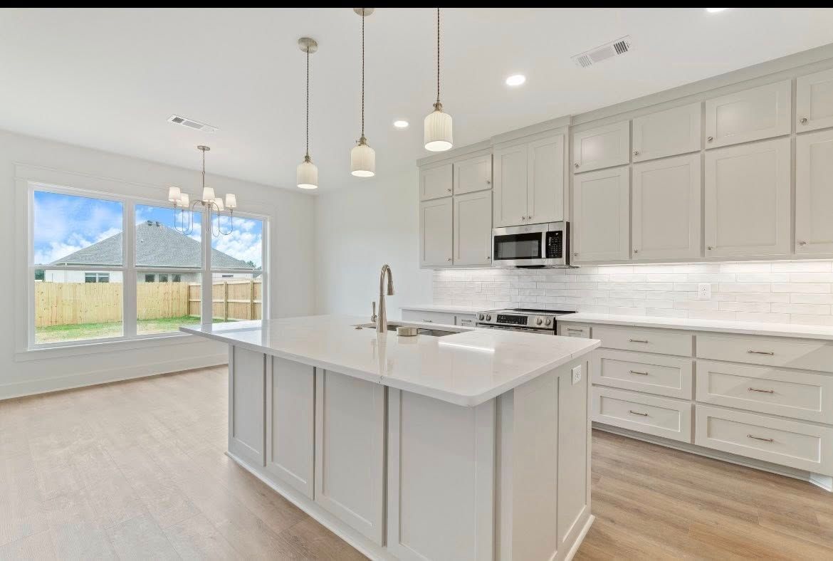 A bright, modern kitchen featuring light gray cabinetry, a large white island with a sink, and pendant lighting.