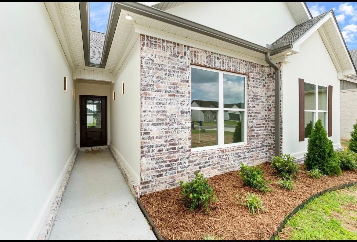A suburban house entrance with a concrete walkway leading to a dark brown front door, beside a whitewashed brick wall.