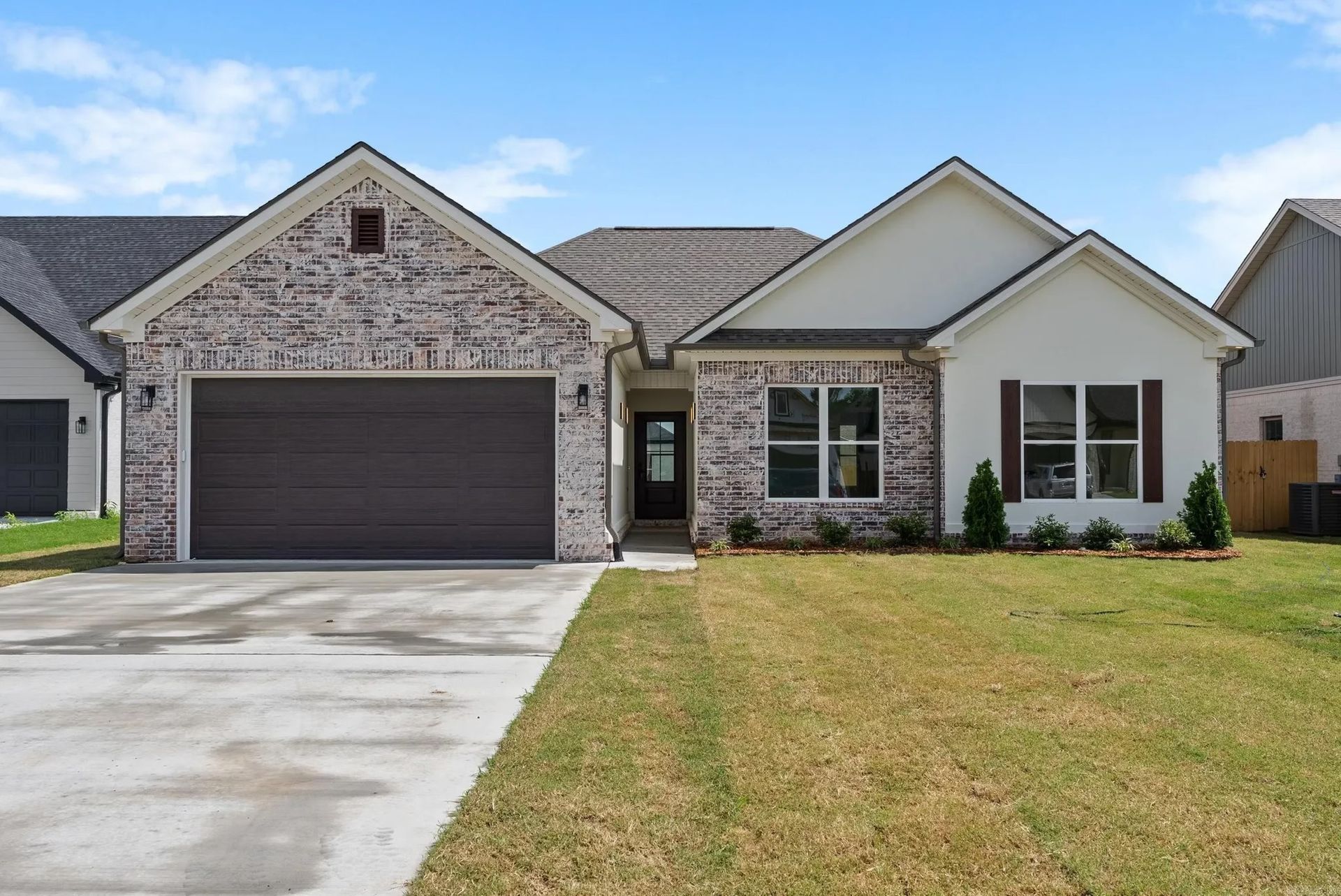 A suburban house with a two-car garage, brick and stucco facade, and a concrete driveway under a partly cloudy sky.