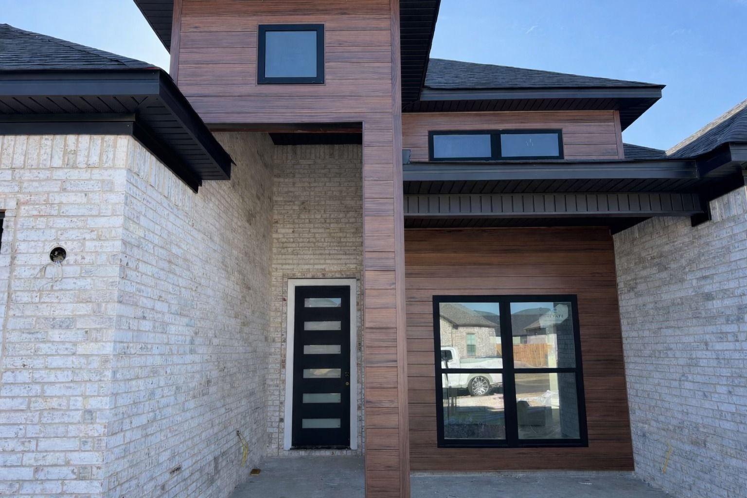 Modern house entrance with white stone siding, dark wood-paneled walls, black-framed windows, and a black front door.