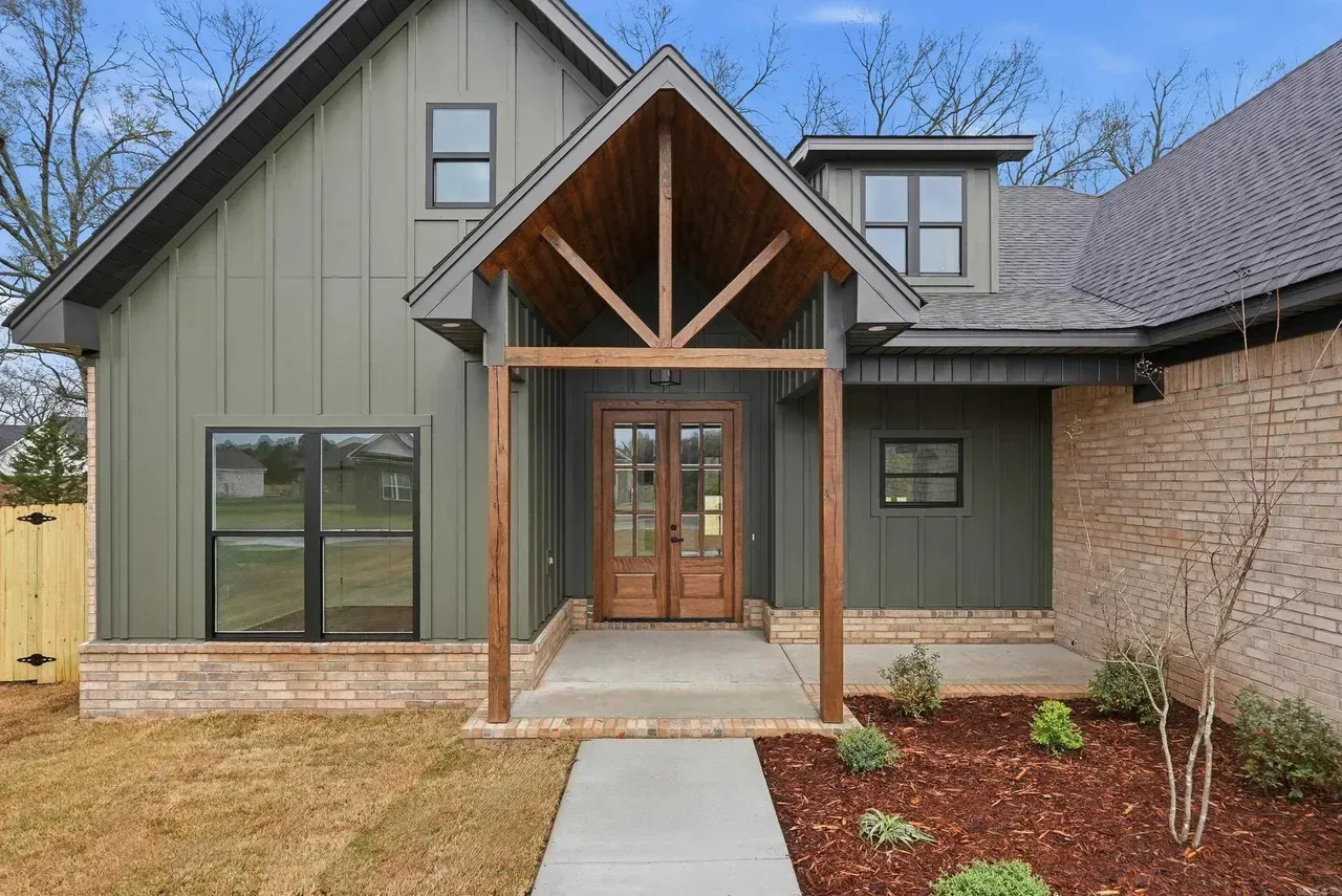 A modern home exterior with olive green vertical siding, a wood-trimmed porch, double glass doors, and a stone facade.