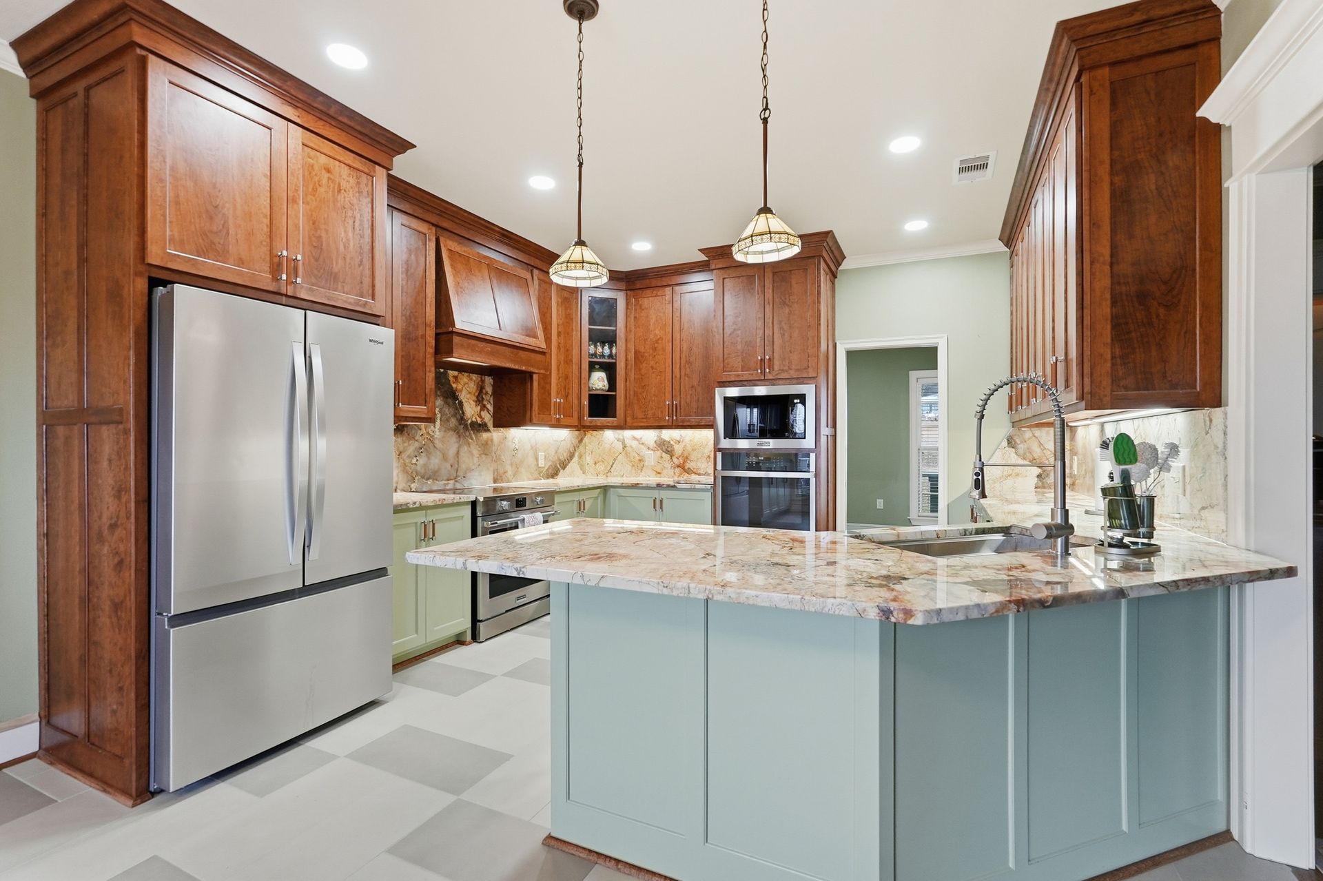 A modern kitchen with wood cabinets, light green island cabinetry, a granite countertop, and stainless steel appliances.