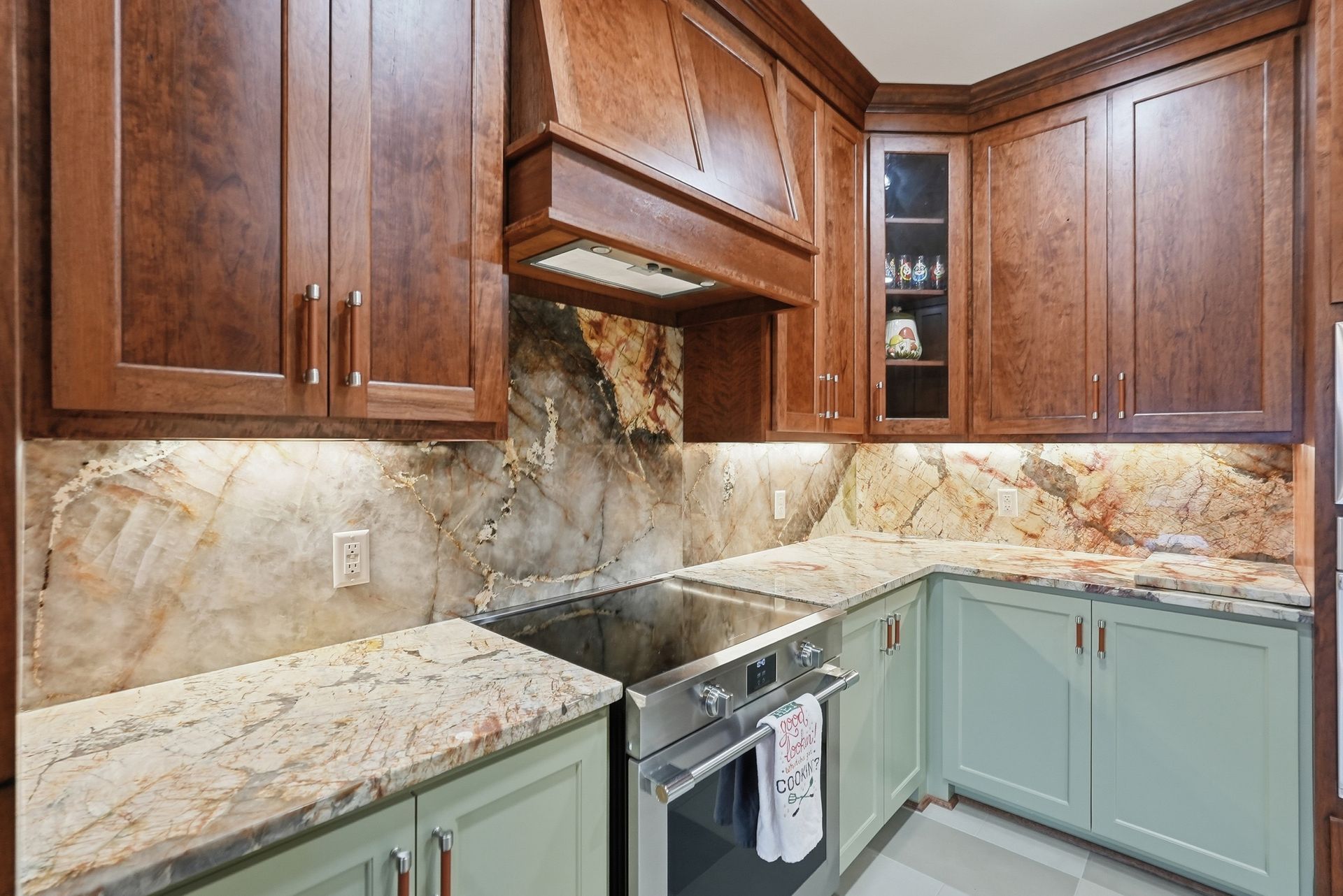 Kitchen with dark wood upper cabinets, light green lower cabinets, granite countertops, and a stone slab backsplash.