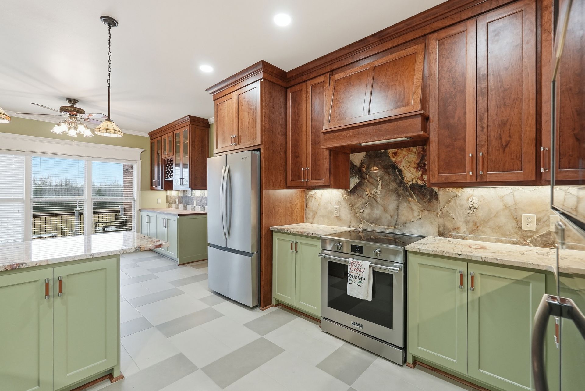 A kitchen with light green lower cabinets, dark wood upper cabinets, granite countertops, and stainless steel appliances.