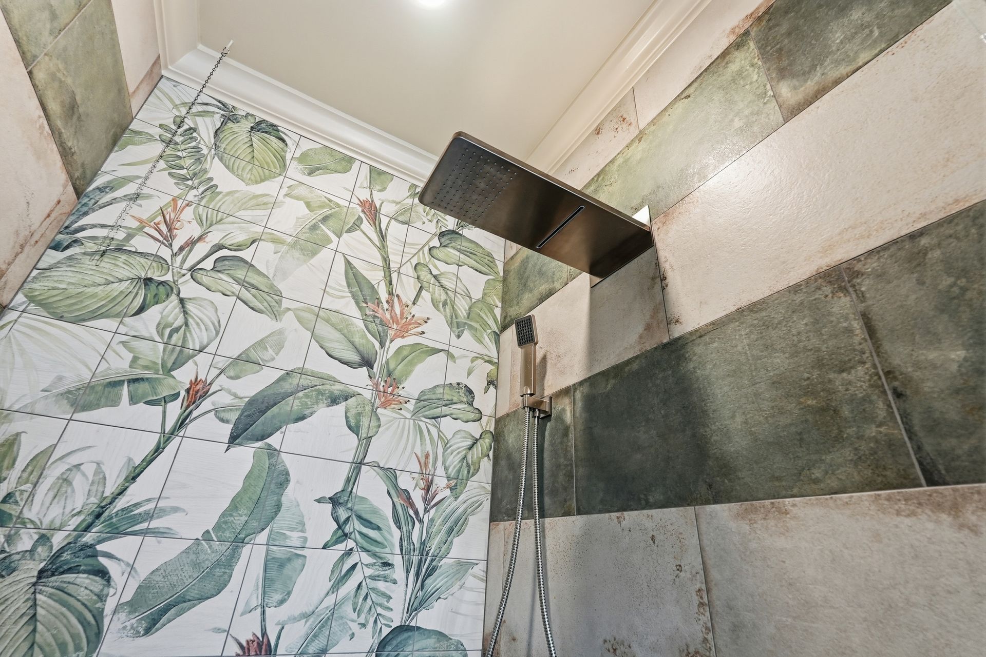 A shower stall features a tiled wall with a vibrant botanical print and an adjacent wall with large, earthy slate tiles.