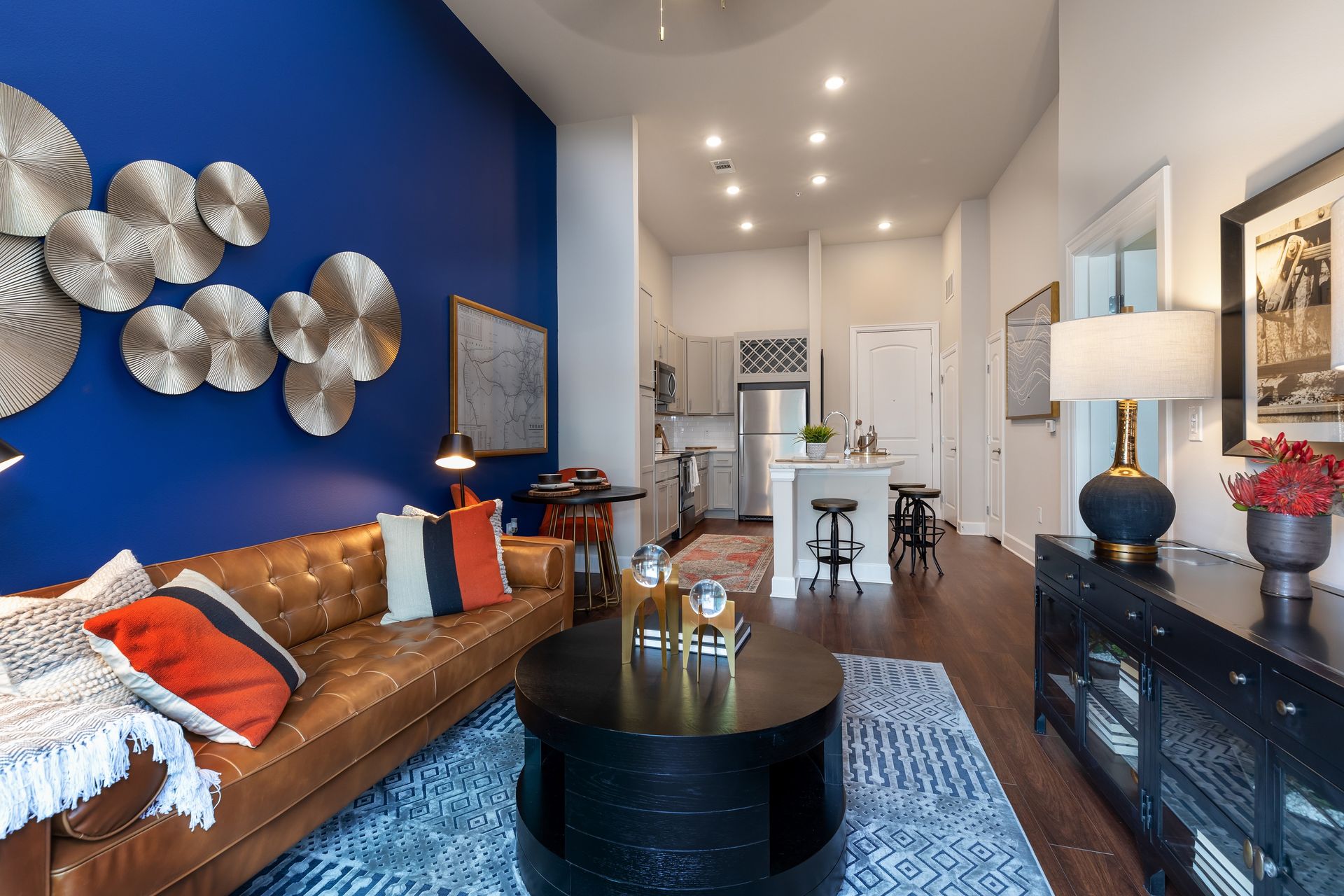 A modern living room with blue walls, a brown leather sofa, and a black coffee table. Kitchen visible in the background.