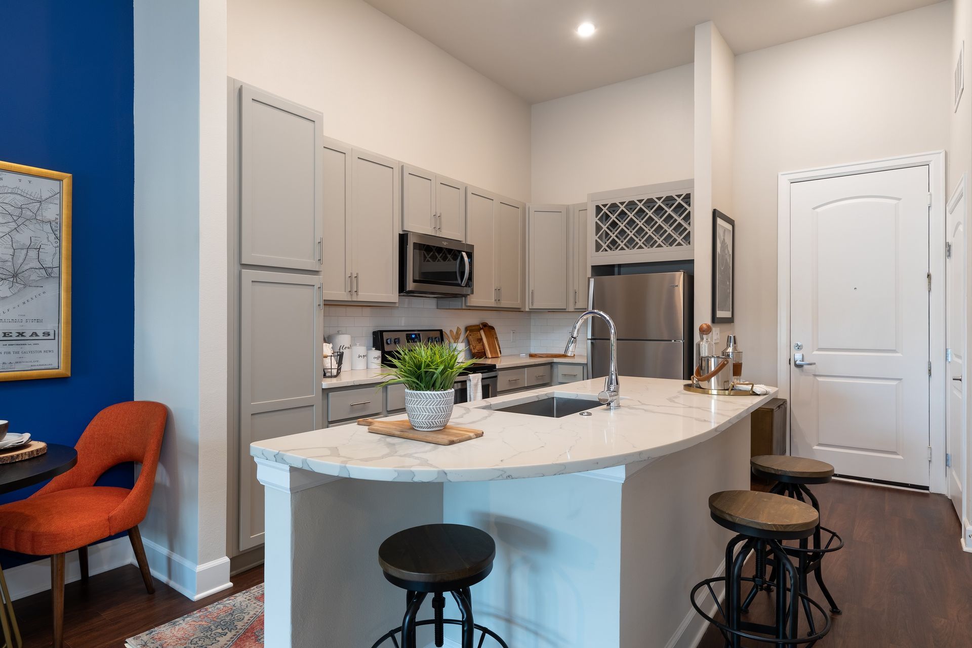 Modern kitchen with gray cabinets, stainless steel appliances, and a white island with stools; a pop of blue wall with art.