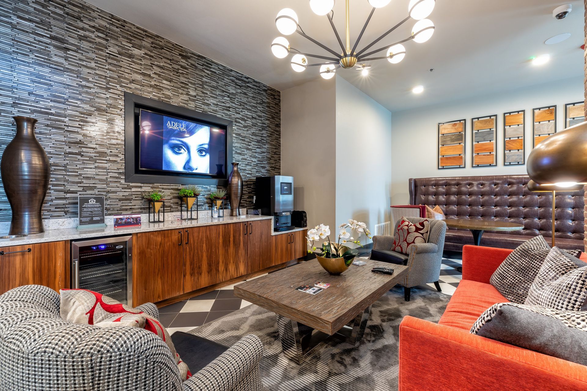 A modern lounge area with a patterned floor, brick accent wall, and various seating arrangements, including an orange couch.