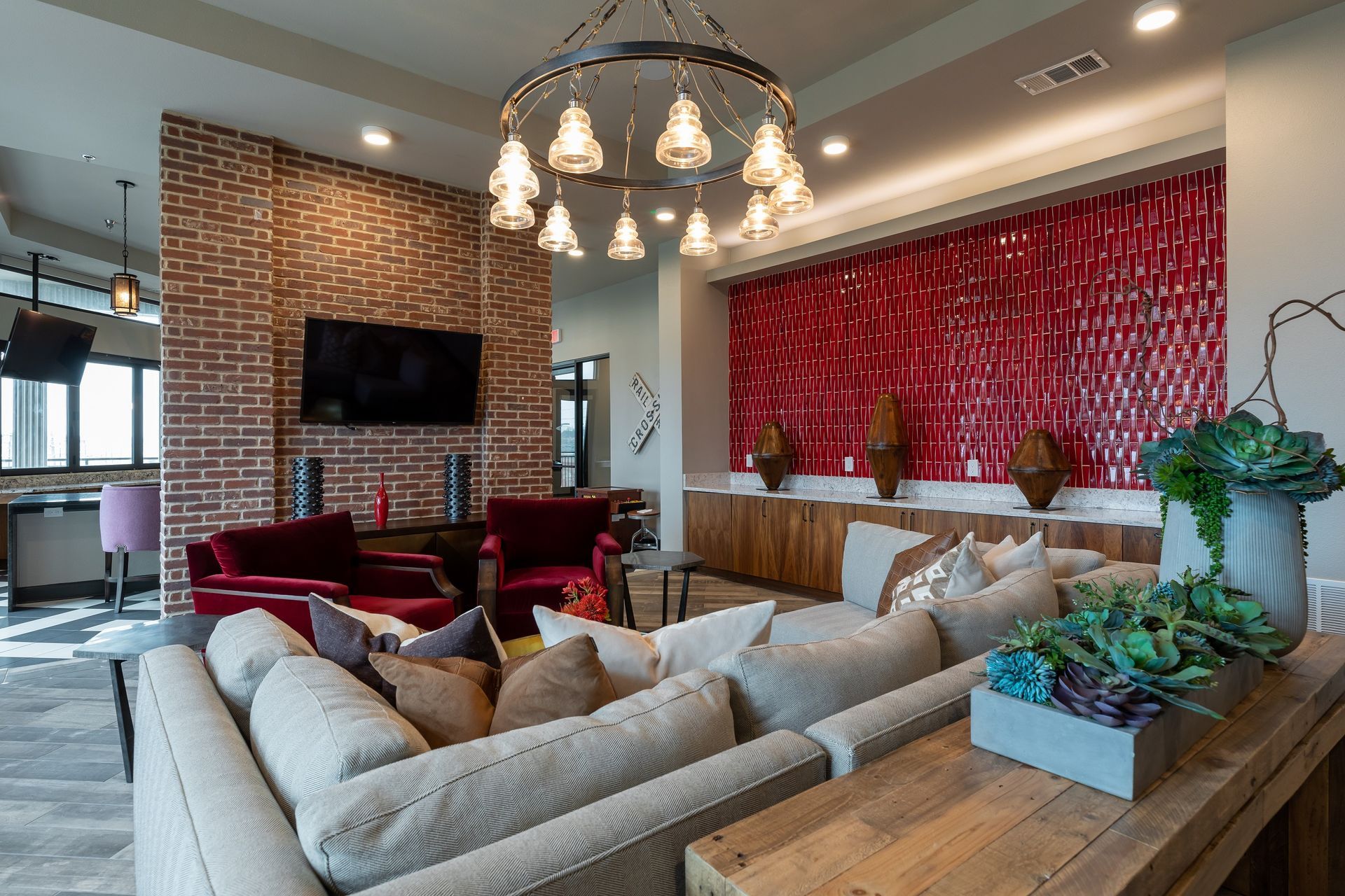 Living room with brick accent wall, red chairs, and large neutral-colored sectional sofa. A red textured wall is in the background with decorative vases and a wood console.