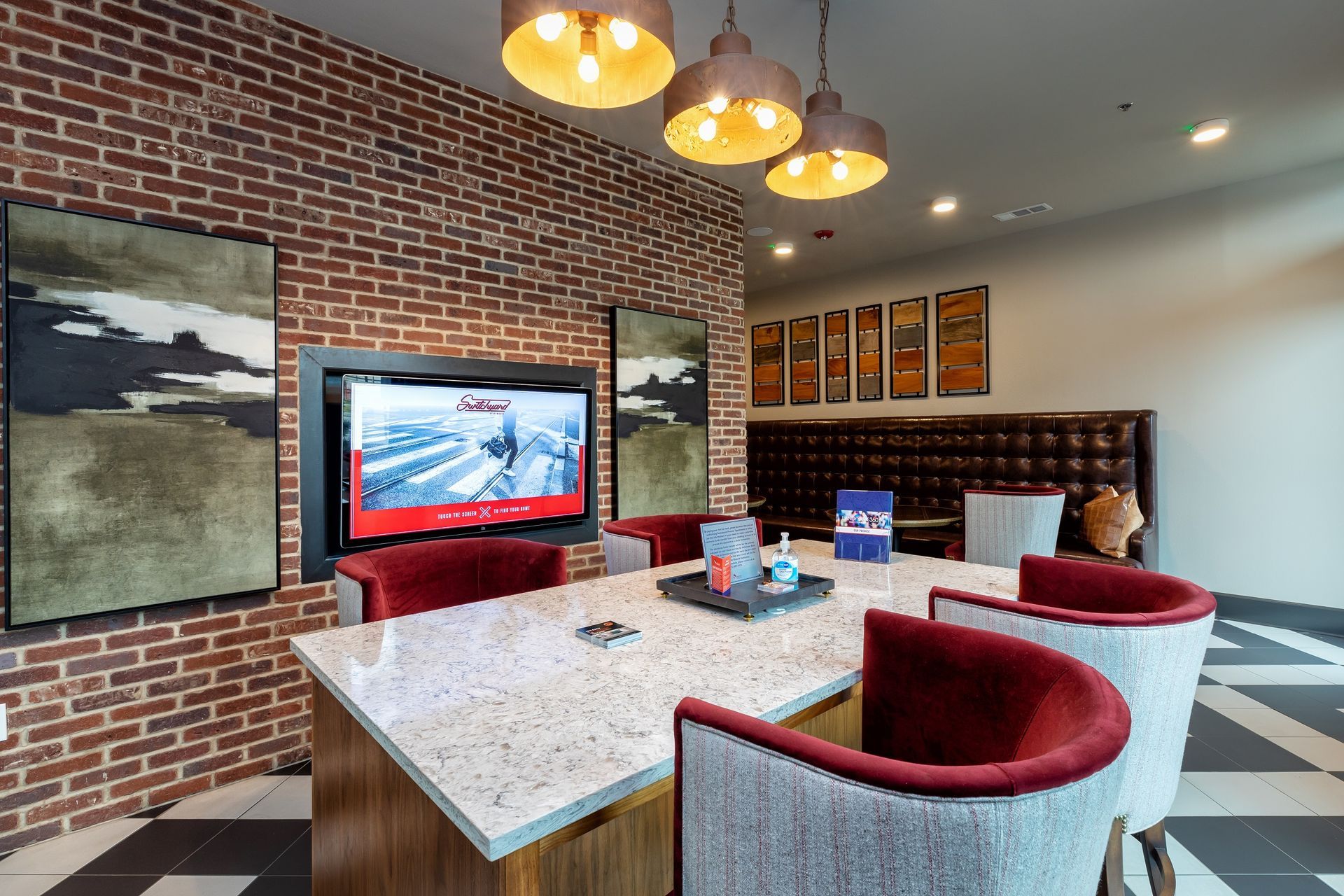 A modern lounge area with a brick wall, TV, table with chairs, and decorative pendant lights.
