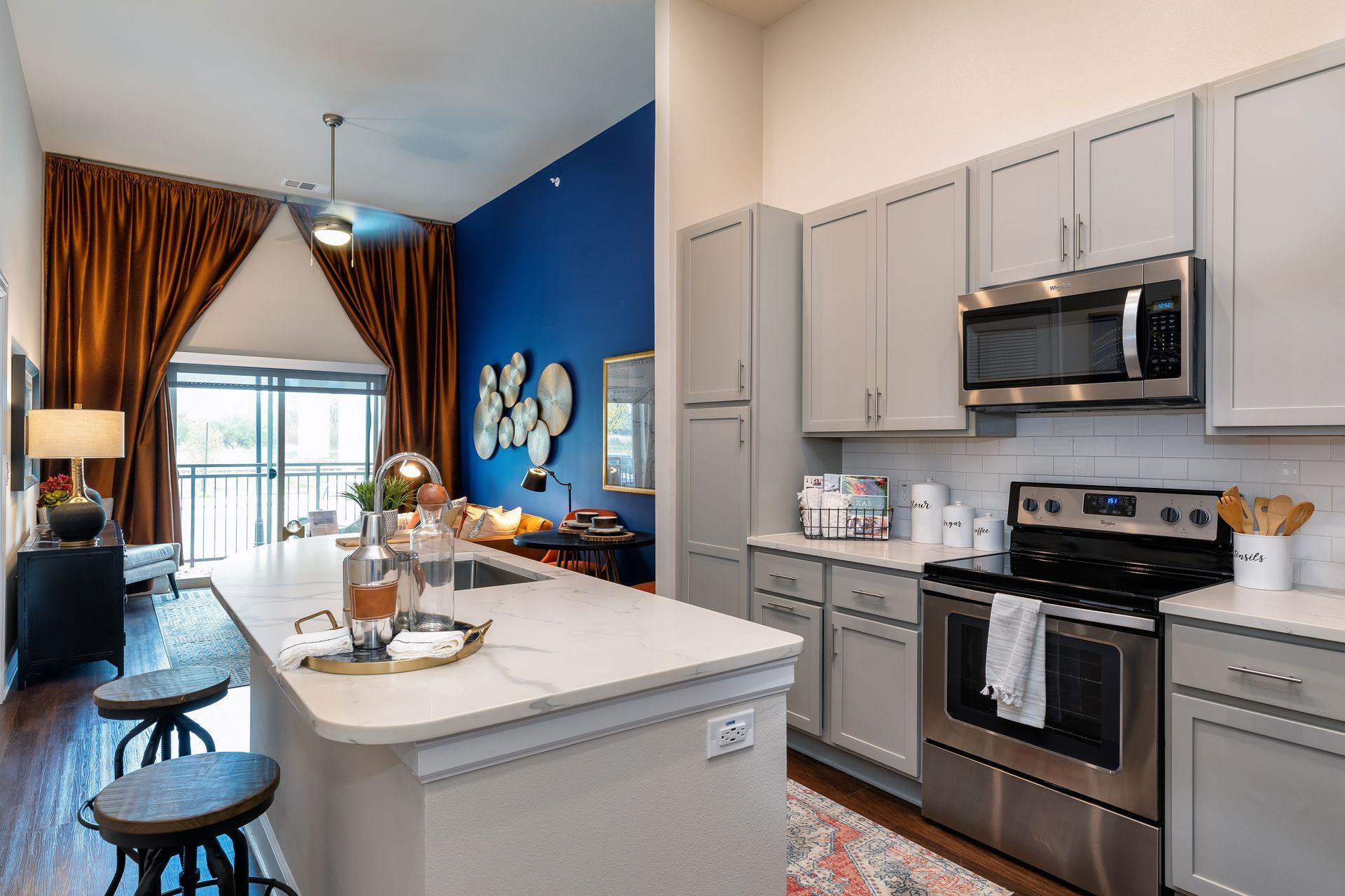 Modern kitchen with gray cabinets, stainless steel appliances, and an island with seating. A dark blue accent wall adds color.
