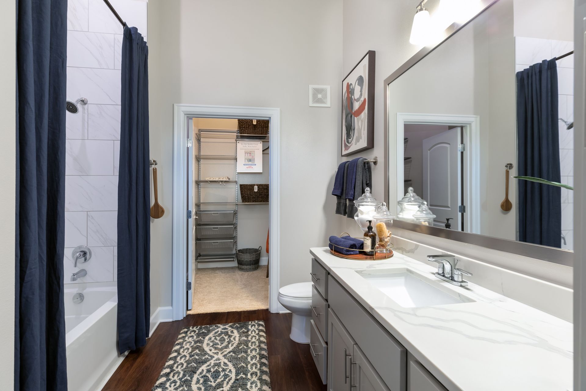 A bathroom with a dark blue shower curtain, gray vanity, and a walk-in closet visible in the background.