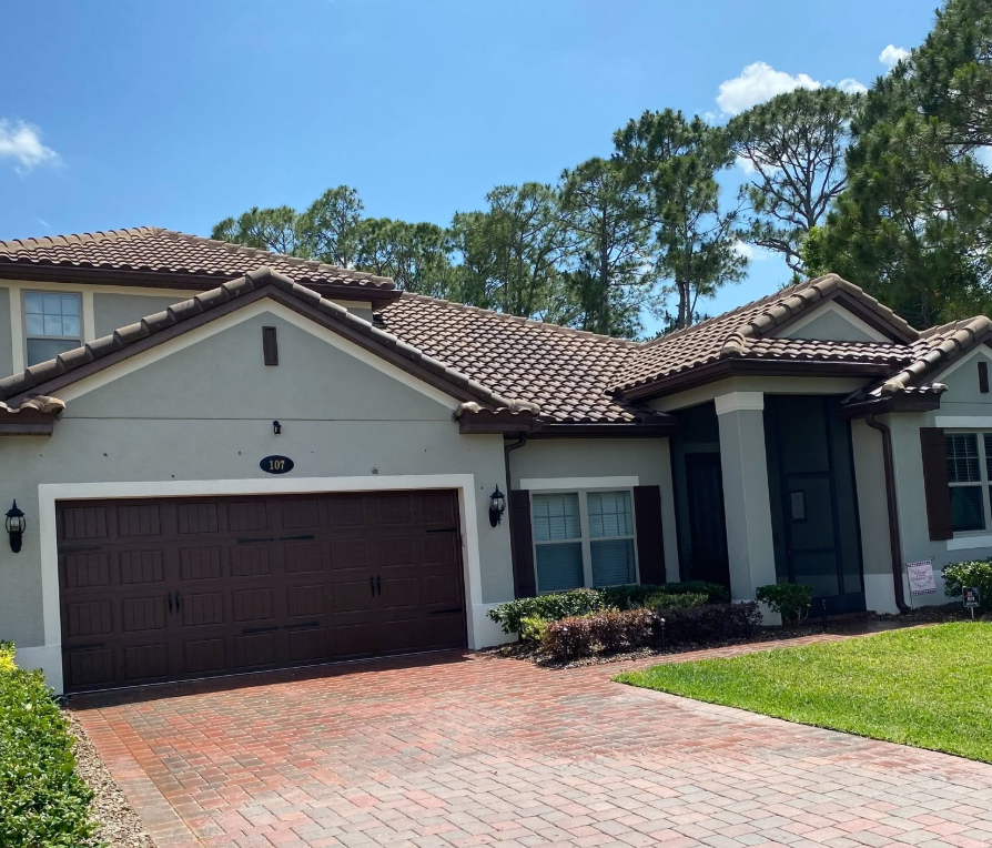 Person power-washing the side of a gray house beneath the roofline