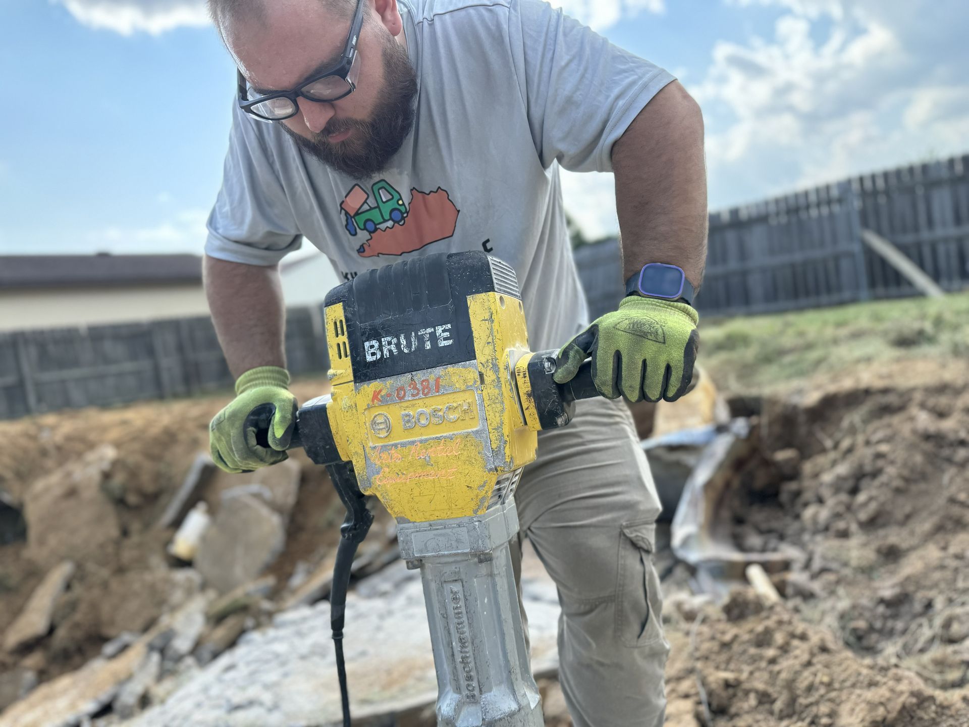 Man using a yellow jackhammer, breaking up concrete outdoors.