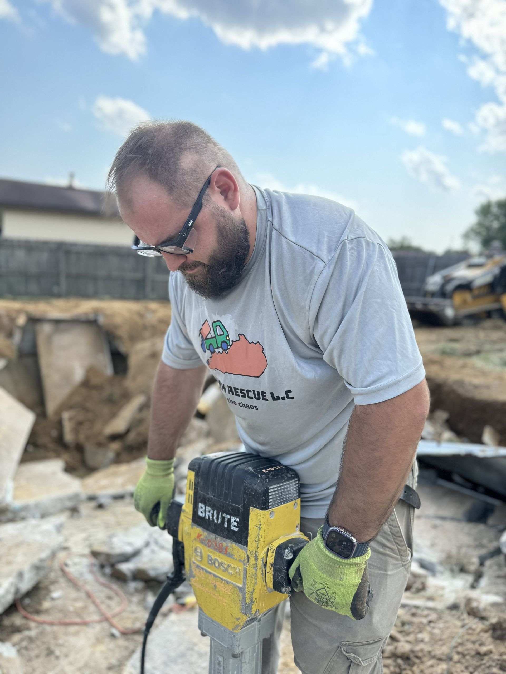 Man using a yellow jackhammer on concrete outdoors, wearing safety glasses and gloves.
