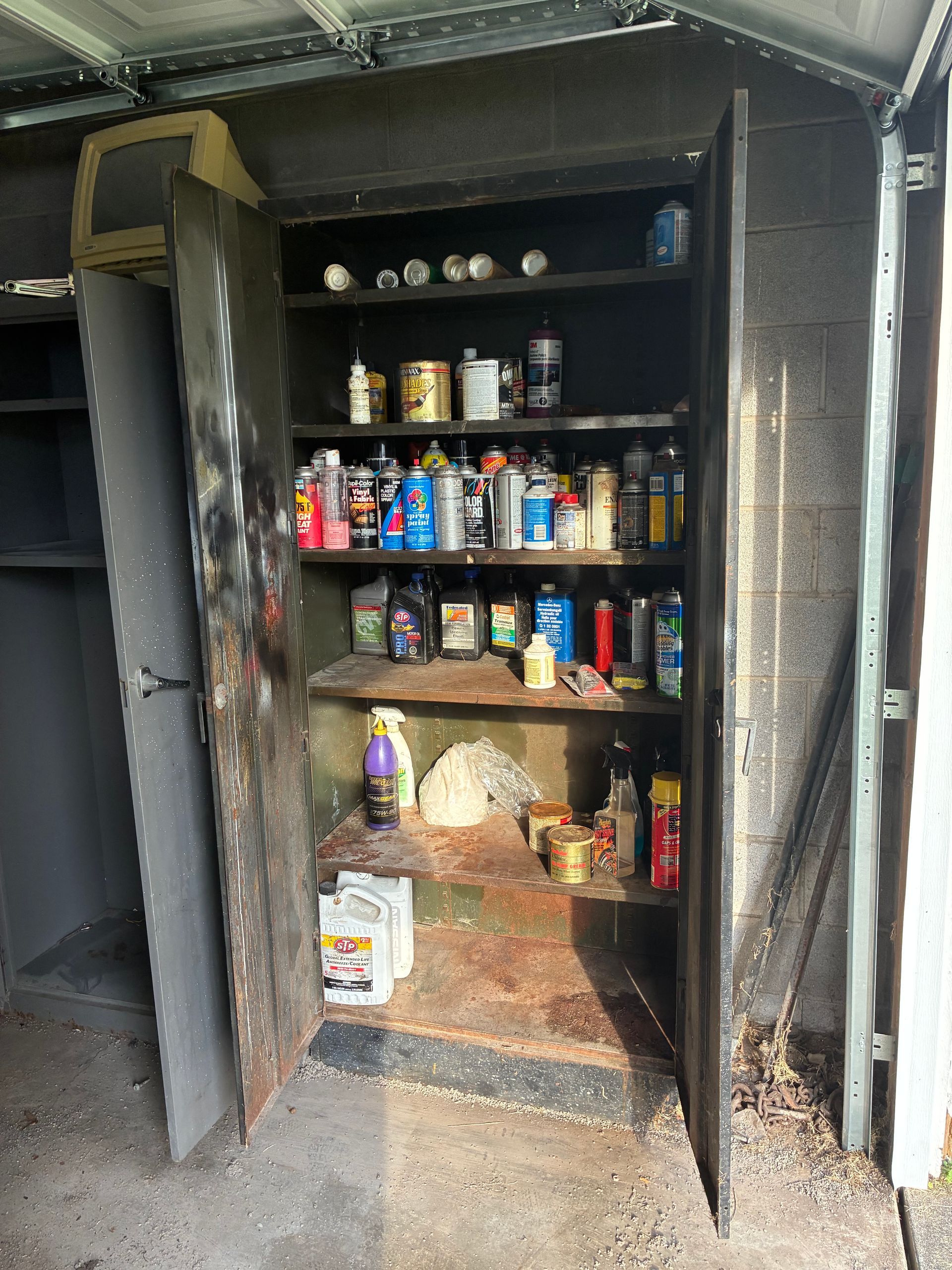 A metal storage cabinet filled with various cans and bottles of chemicals in an outdoor setting.