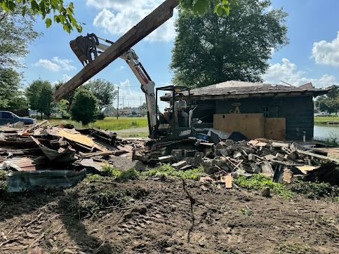 Demolition of a small building by an excavator. Debris and dirt surround the structure.