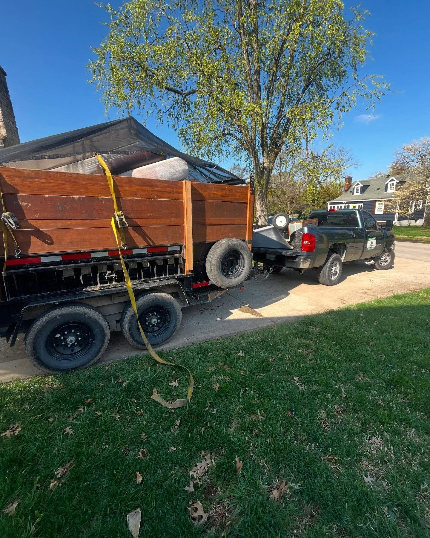 Black pickup truck towing a trailer with a wooden bed on a grassy area, under a blue sky.