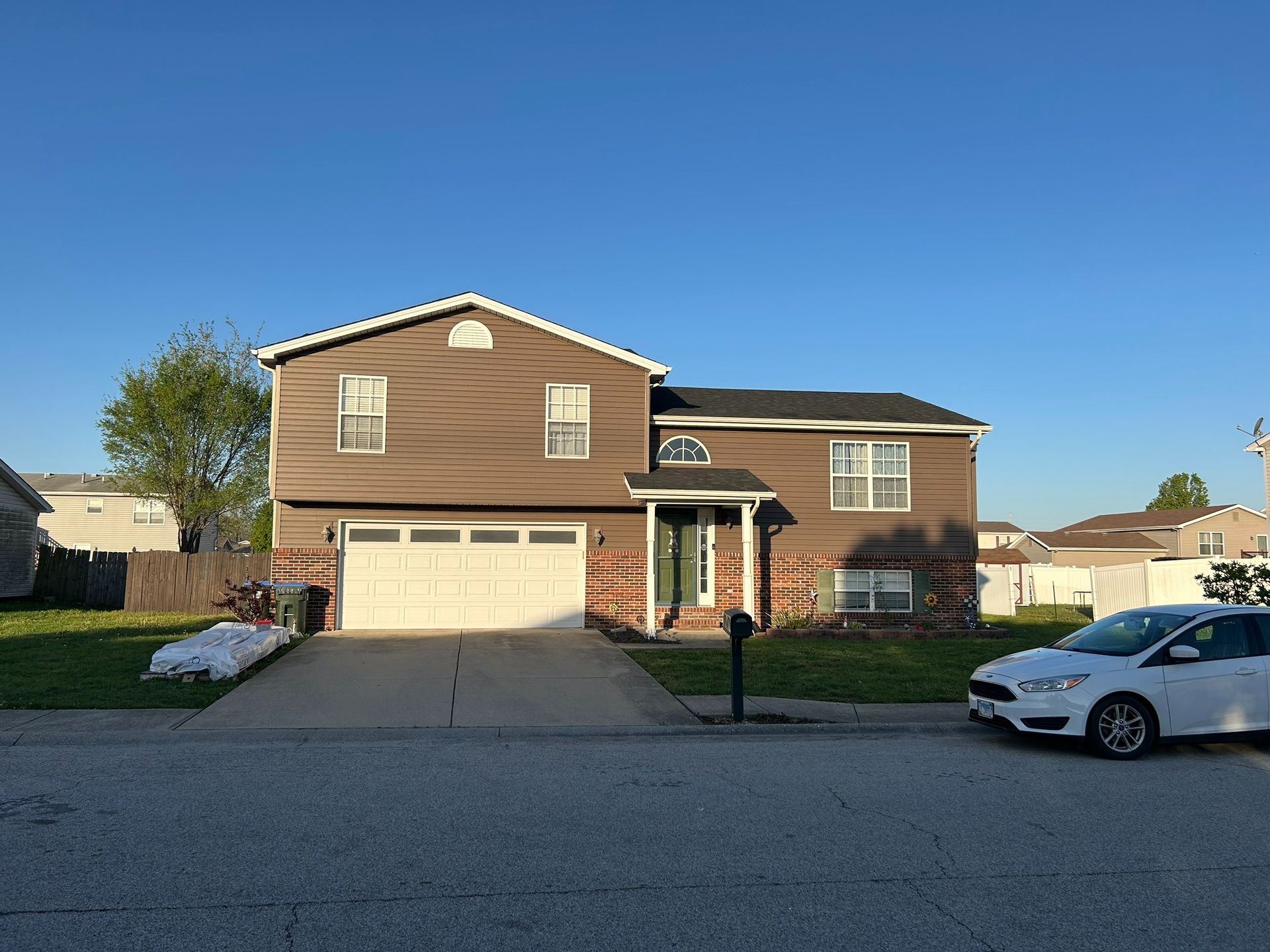 Brown two-story house with a white garage door, a driveway, and a parked white car on a sunny day.
