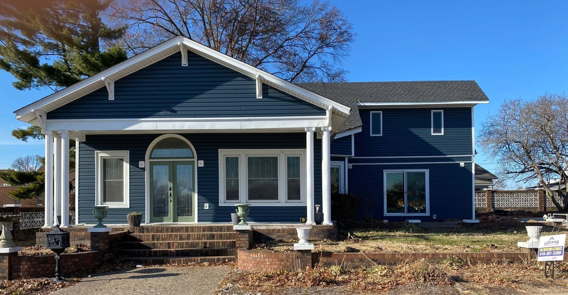 Blue house with white trim, covered porch, and columns on a sunny day.
