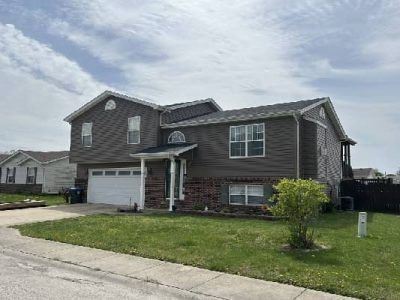 Brown two-story house with a white garage door, surrounded by grass and a cloudy sky.