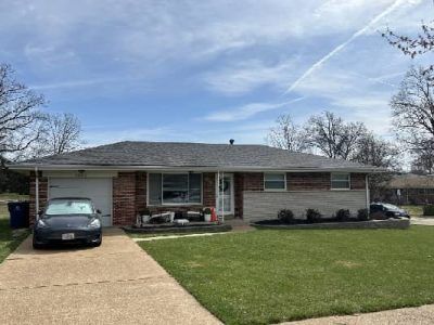 Single-story brick house with attached garage, a car in the driveway, and a well-kept lawn under a cloudy sky.