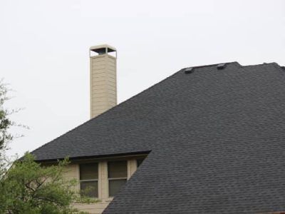 Dark roof with a chimney, windows, and a gray sky.