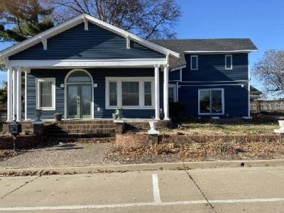 Blue house with white trim, covered porch, and front door, on a sunny day.