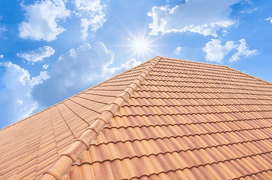Terracotta tile roof with sun and blue sky with clouds.