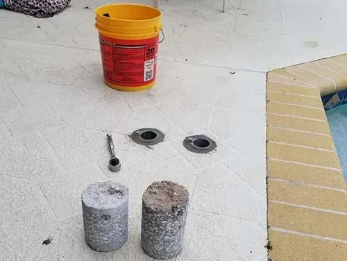 A yellow bucket and two concrete cylinders are on the floor next to a pool.