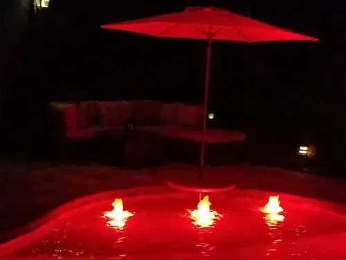 A red umbrella is sitting in the middle of a pool at night.