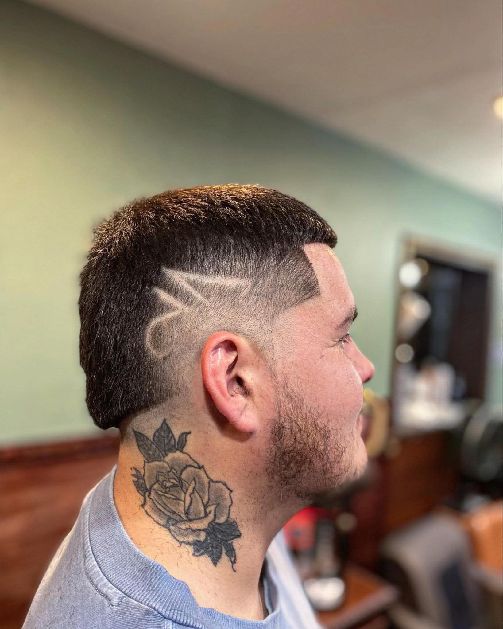 A side profile of a man with a short mohawk hairstyle featuring a shaved, zigzag hair design and a rose neck tattoo.