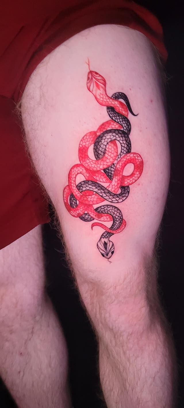 A tattoo on a person's upper thigh featuring two intertwined snakes, one in red ink and the other in black ink.