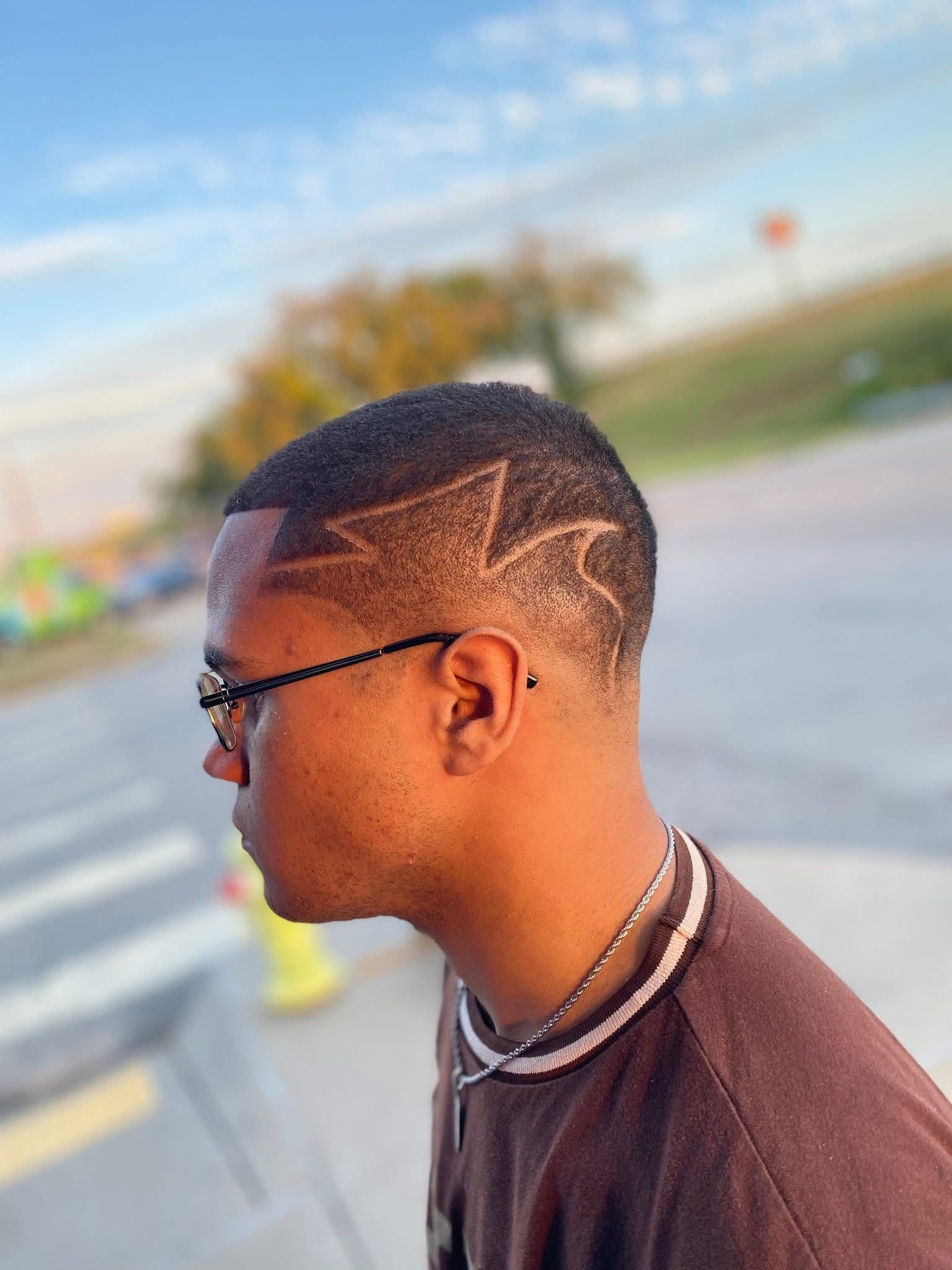Side view of a person with a short, faded haircut featuring a shaved, zigzag lightning bolt design on the side.