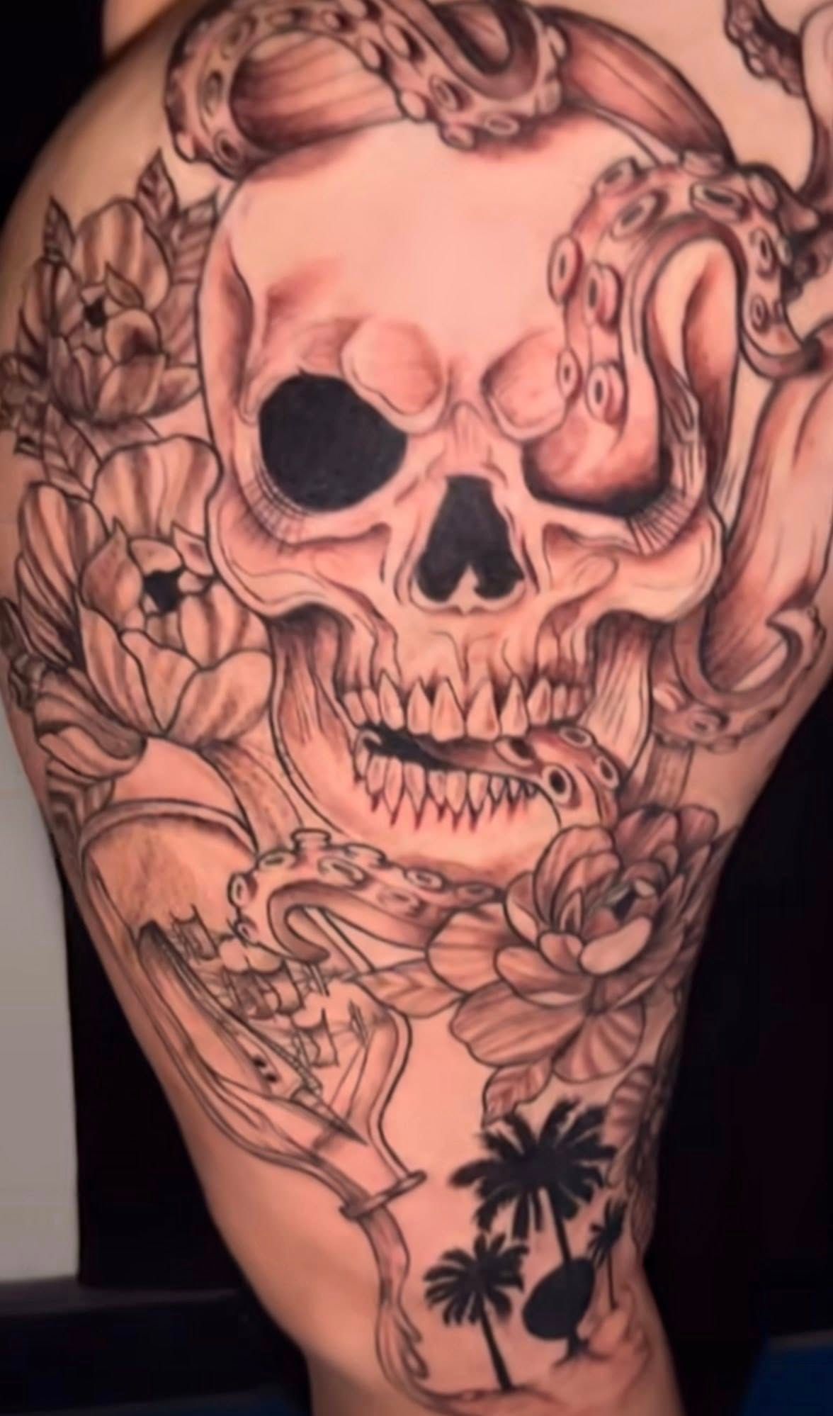 Black-and-gray tattoo featuring a skull intertwined with octopus tentacles, flowers, a message in a bottle, and palm trees.