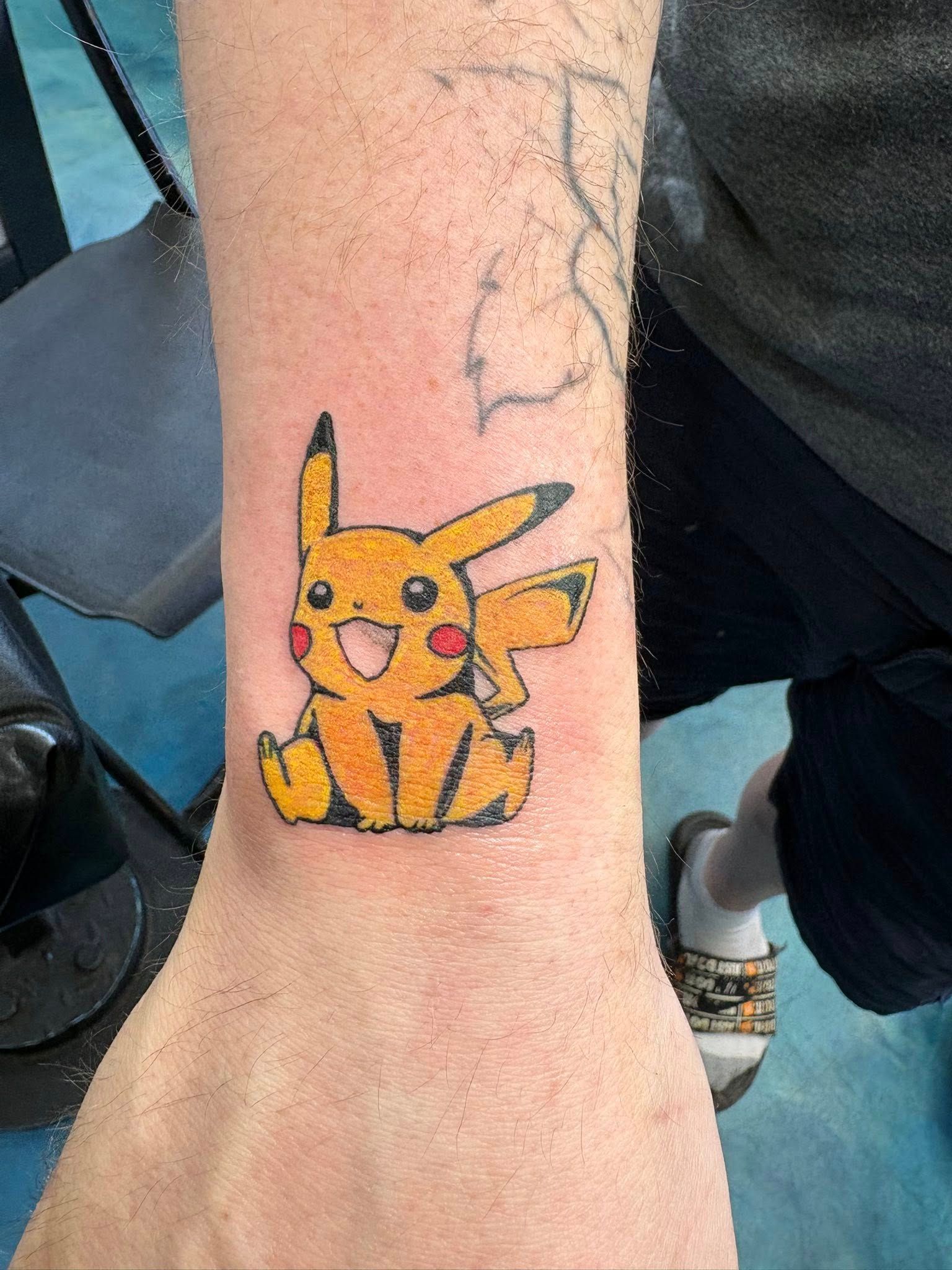 A tattoo of a cheerful, yellow Pikachu sitting on a person's inner forearm.