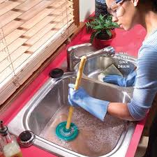 Overhead shot of a woman plunging her kitchen sink because its clogged.