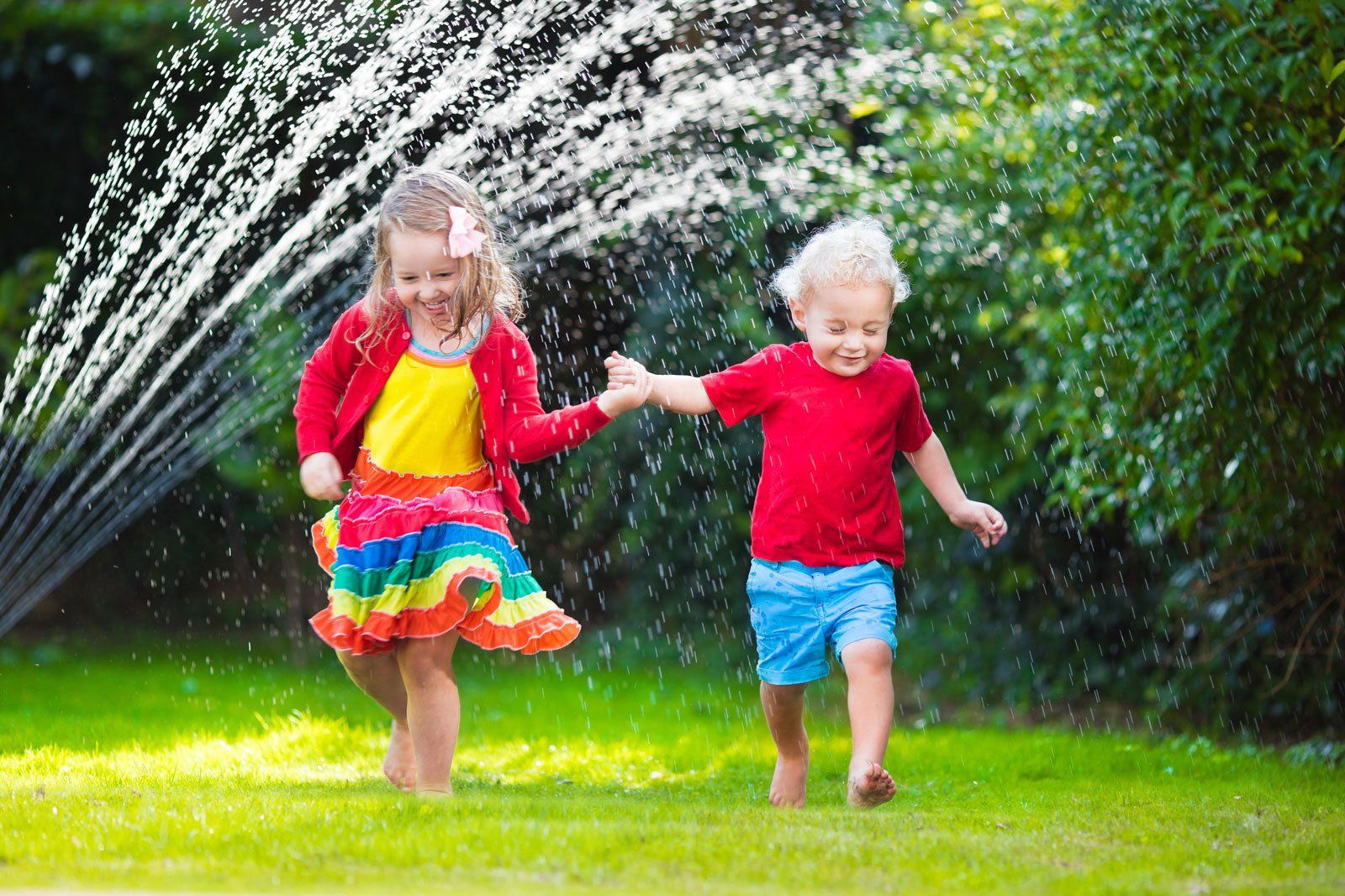 2 Kids playing in the sprinkler in the summer
