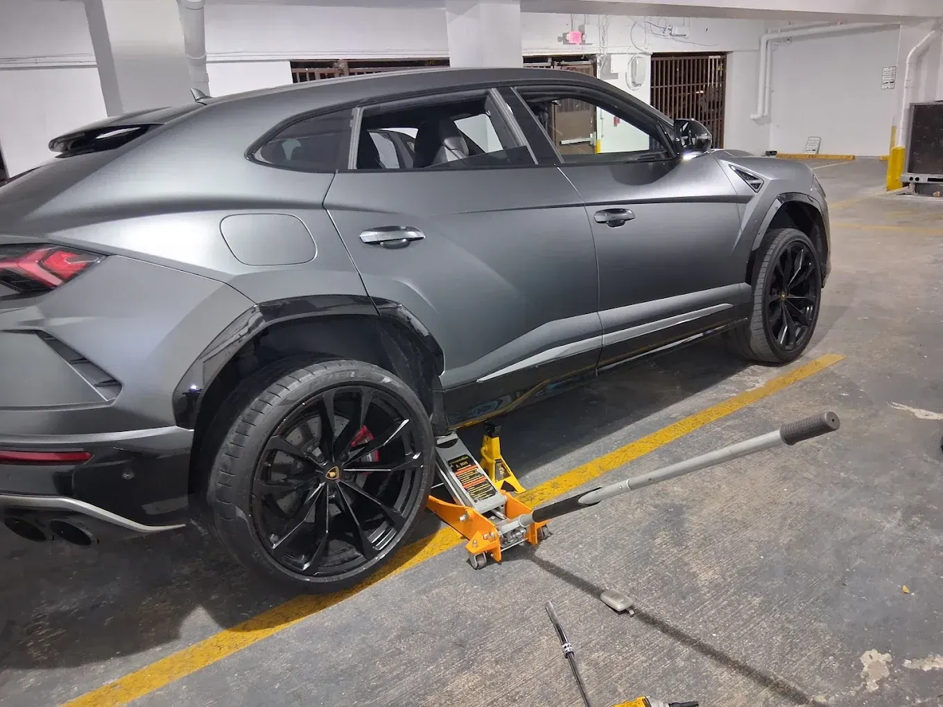 Gray SUV with black rims parked in a garage, secured by a wheel clamp.