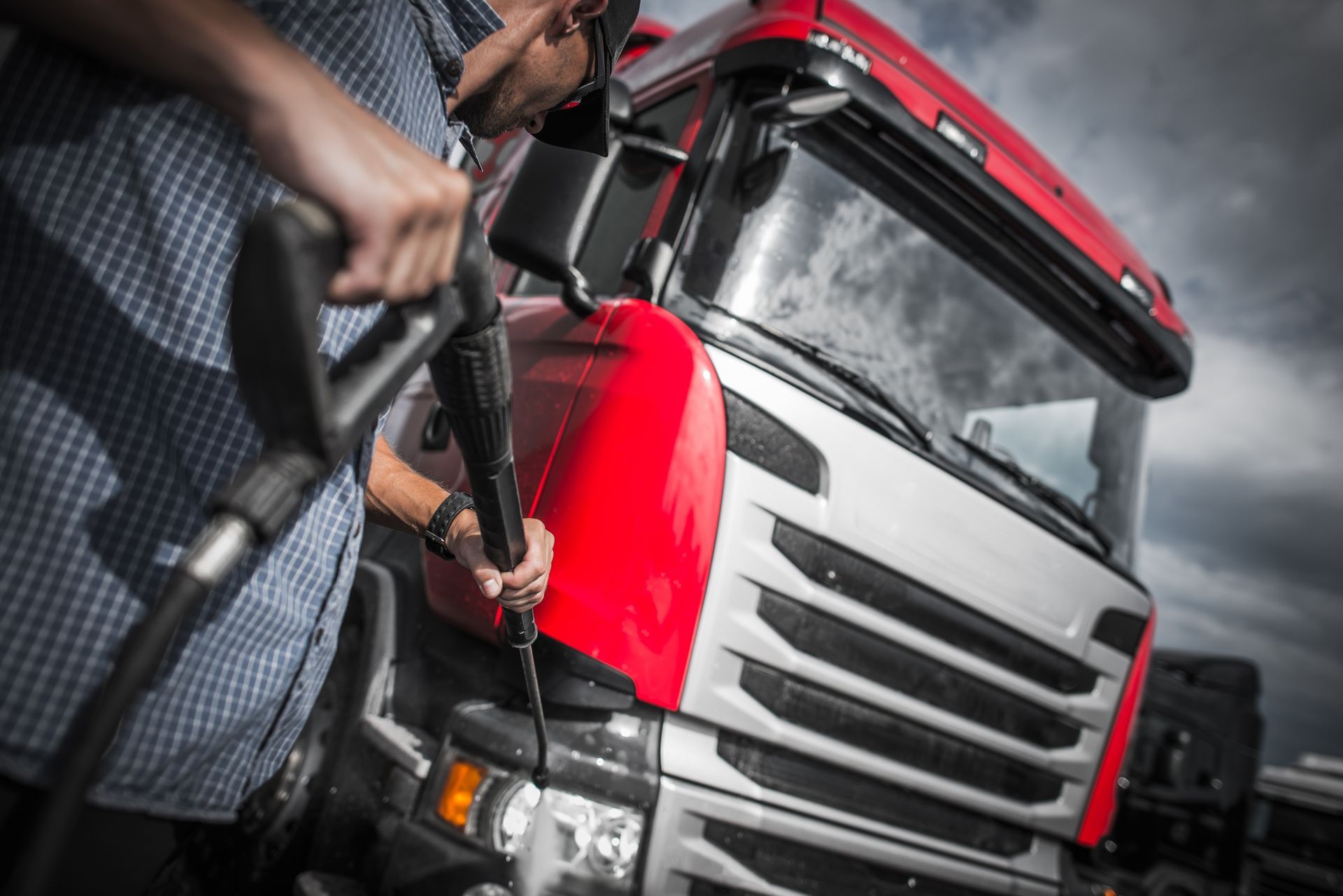 A man is cleaning a red and white truck with a high pressure washer.