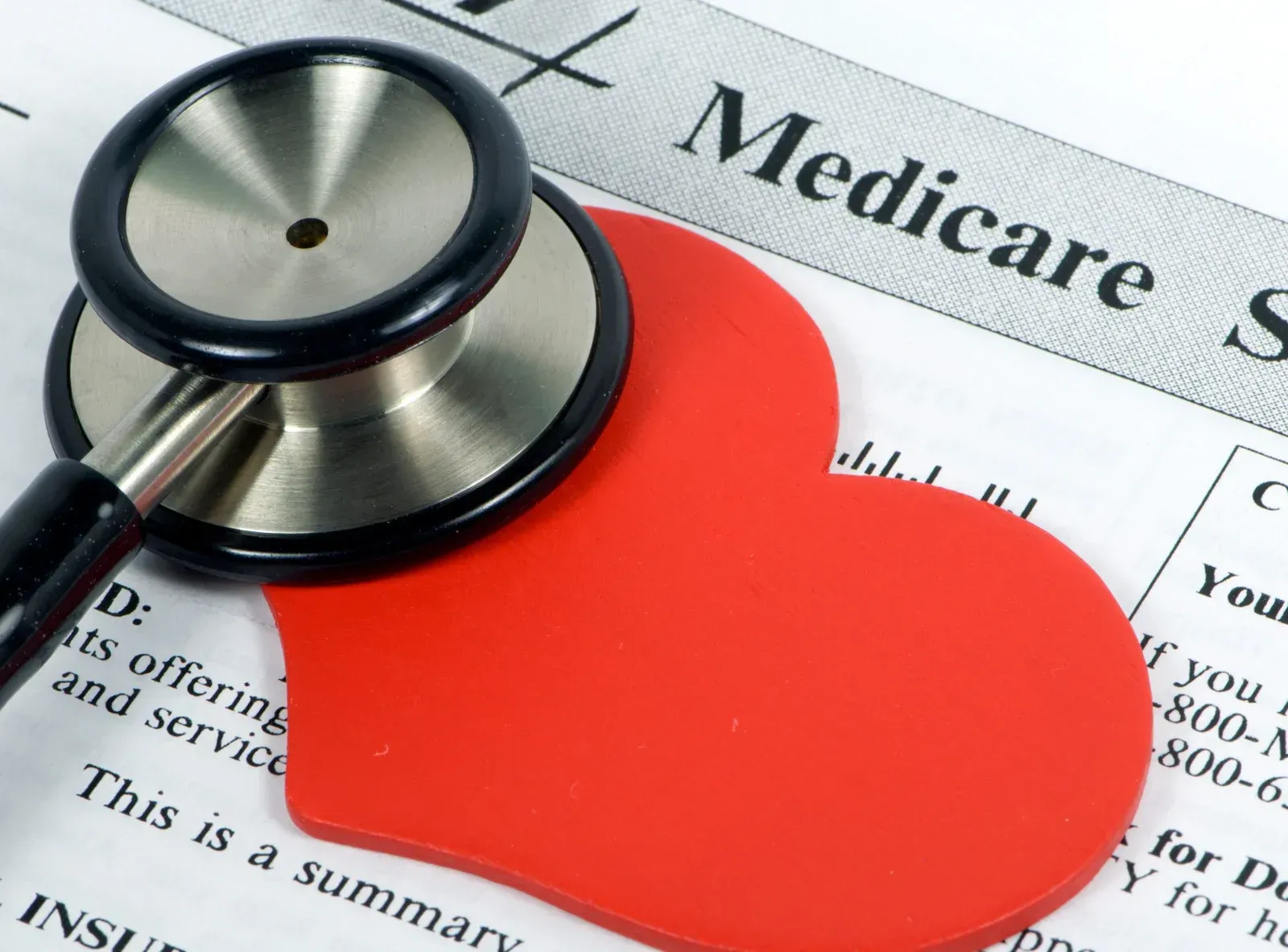 Stethoscope on a red heart shape, lying on a Medicare document summary.
