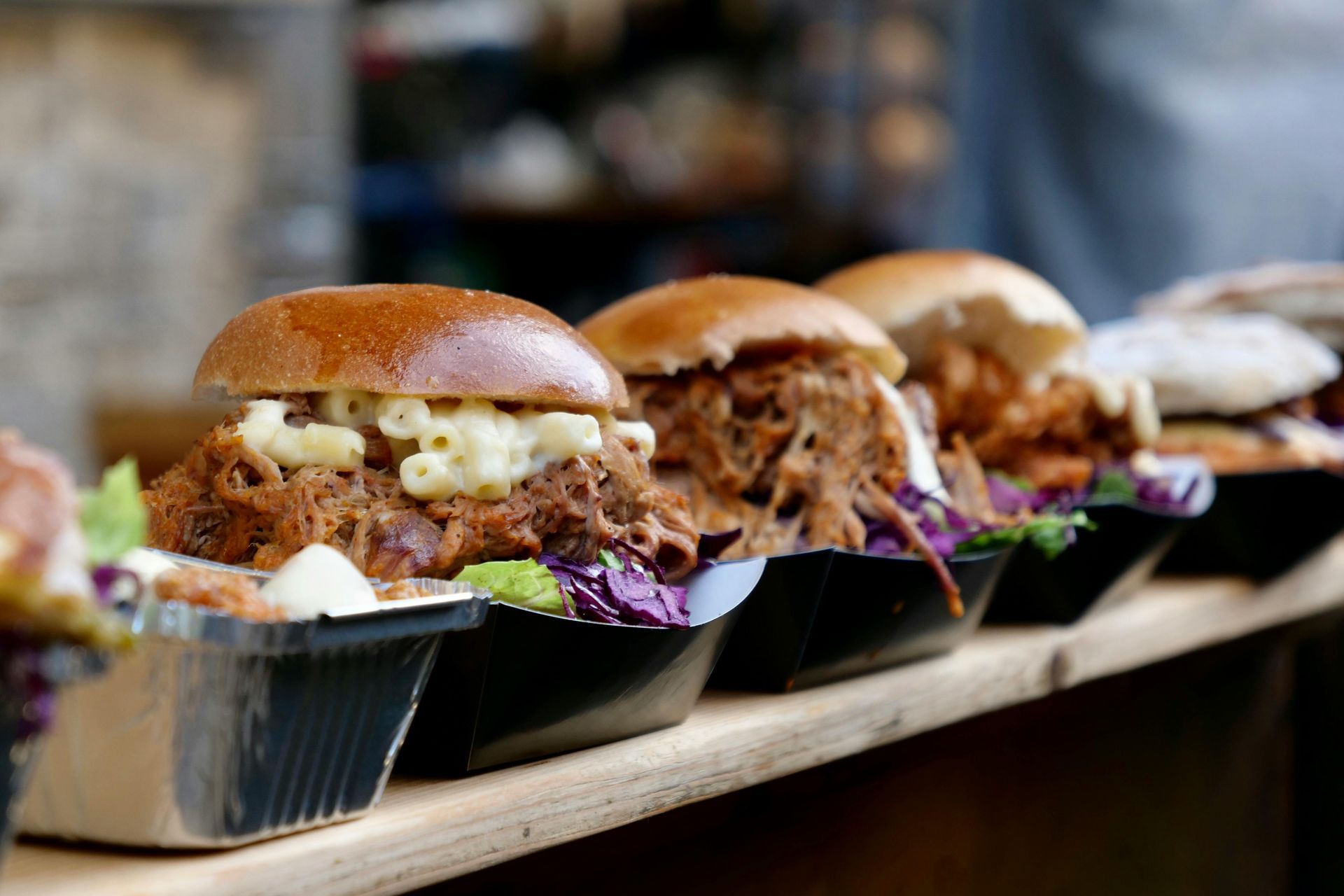A row of pulled pork sandwiches are sitting on a wooden shelf.
