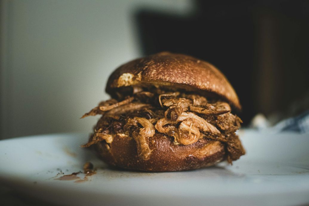 A pulled pork sandwich is sitting on a white plate.